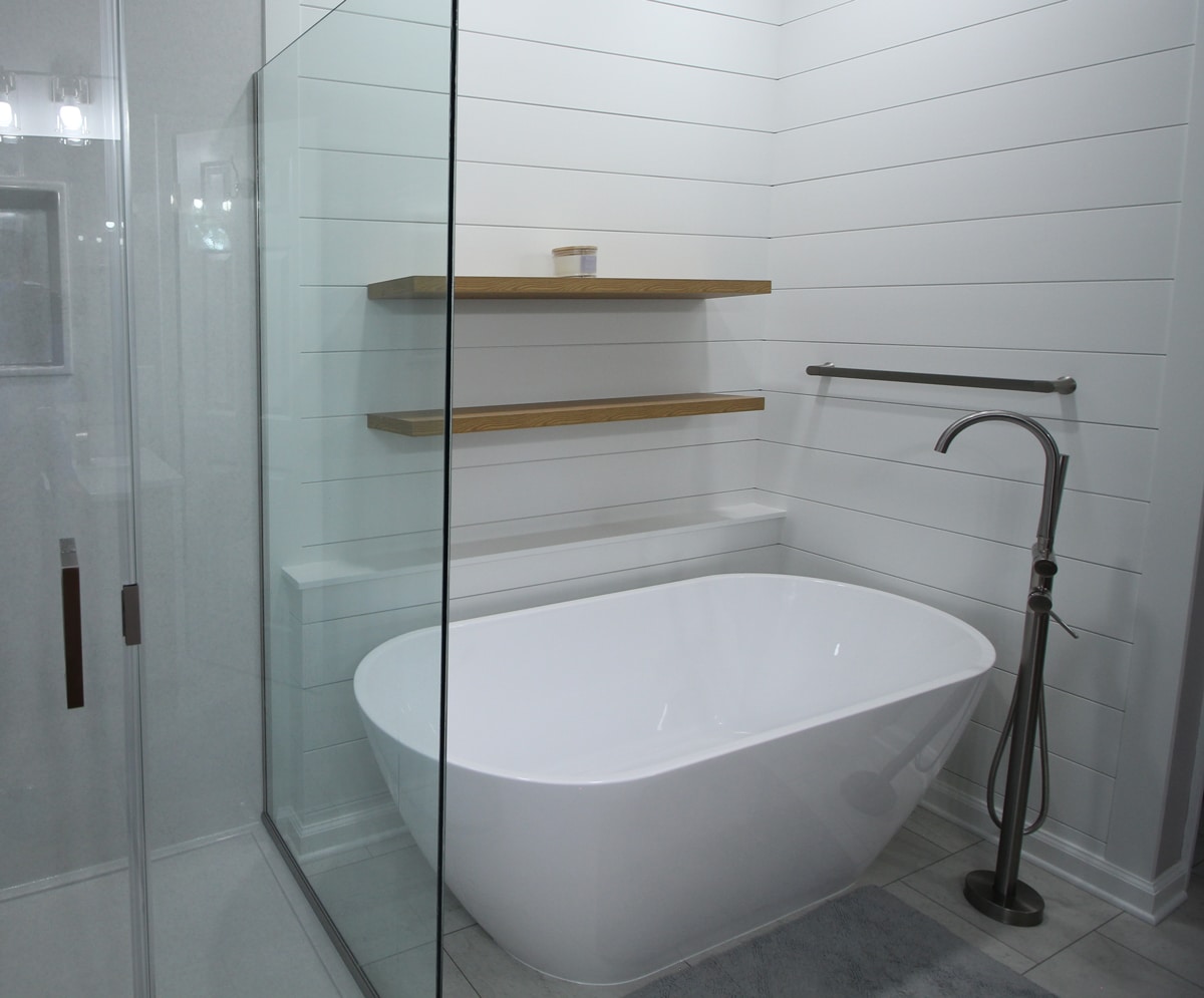 Modern bathroom featuring a white freestanding tub, glass shower, shiplap walls, floating shelves, towel bar, and silver tub filler.