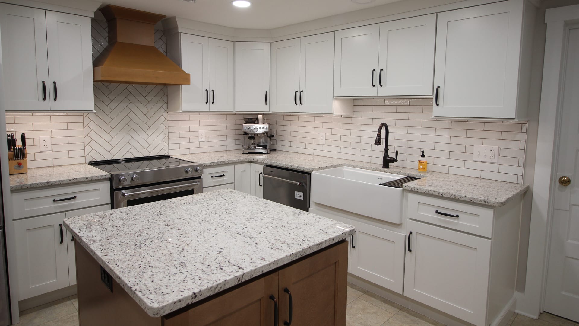 Modern kitchen with white cabinets, granite counters, central island, stainless appliances, farmhouse sink, and copper range hood.