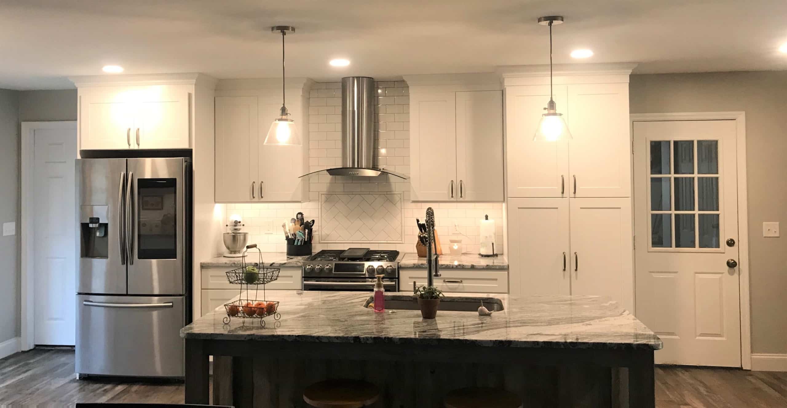 Modern kitchen with white cabinets, stainless appliances, marble island, pendant lights, glass door, and small plants on the island.