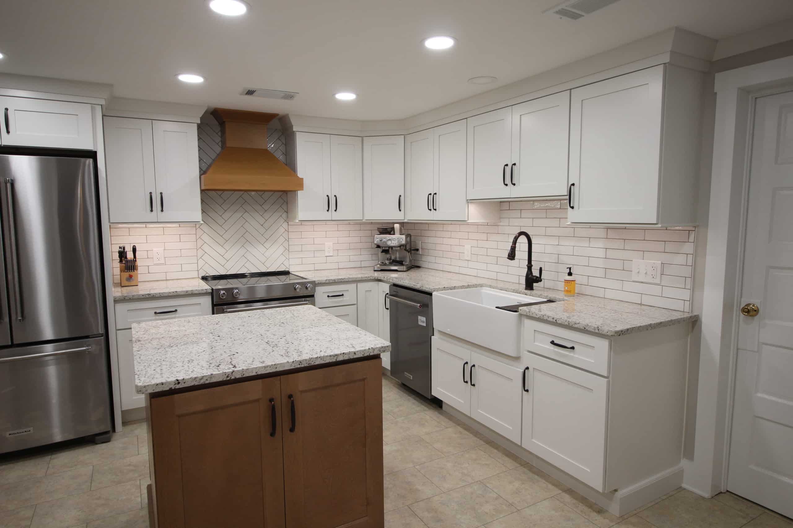 Modern kitchen with white cabinets, granite counters, stainless appliances, farmhouse sink, tiled backsplash, island, bright lights.