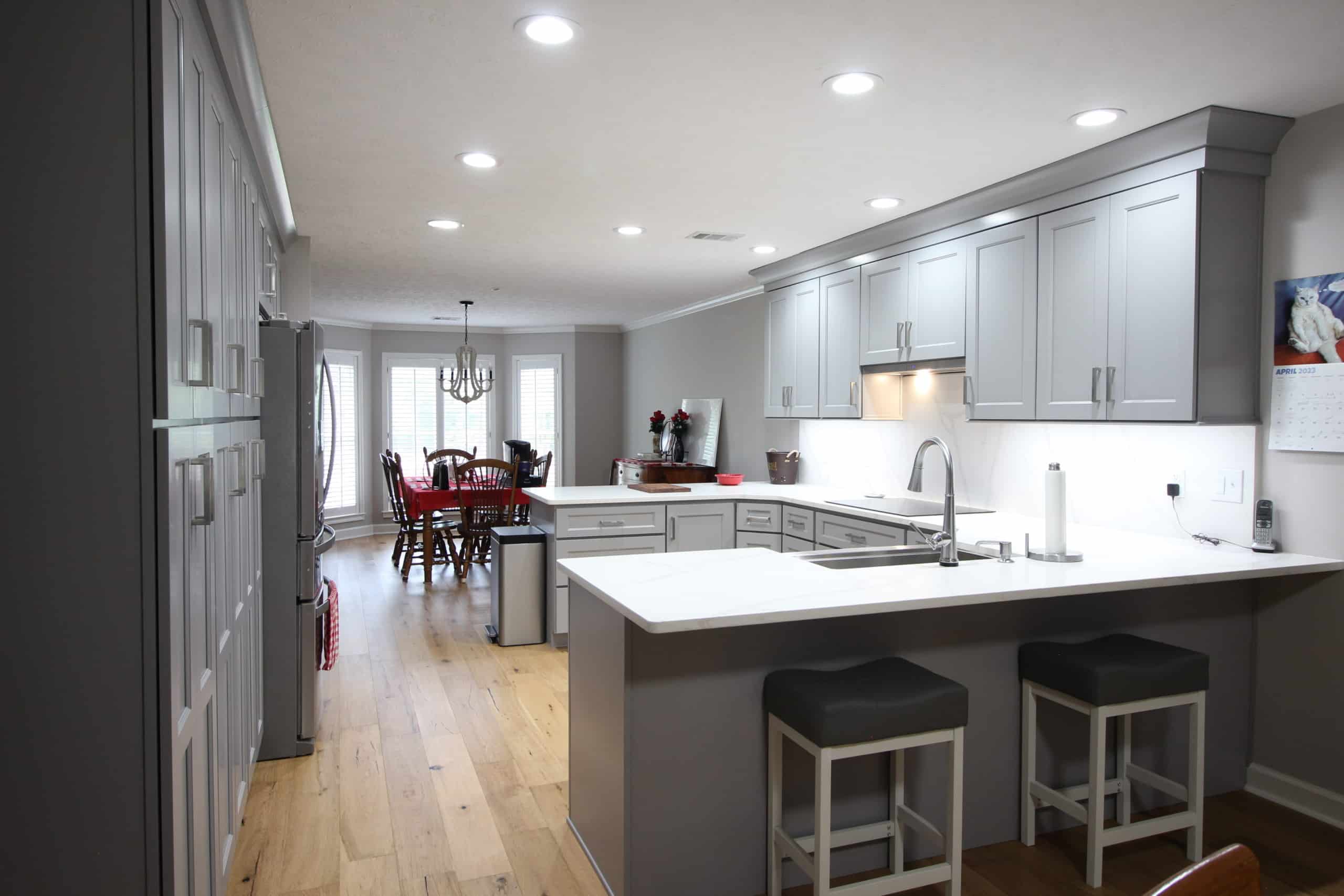 Modern kitchen with gray cabinets, white counters, island with stools, stainless appliances, hardwood floor, and nearby dining area.