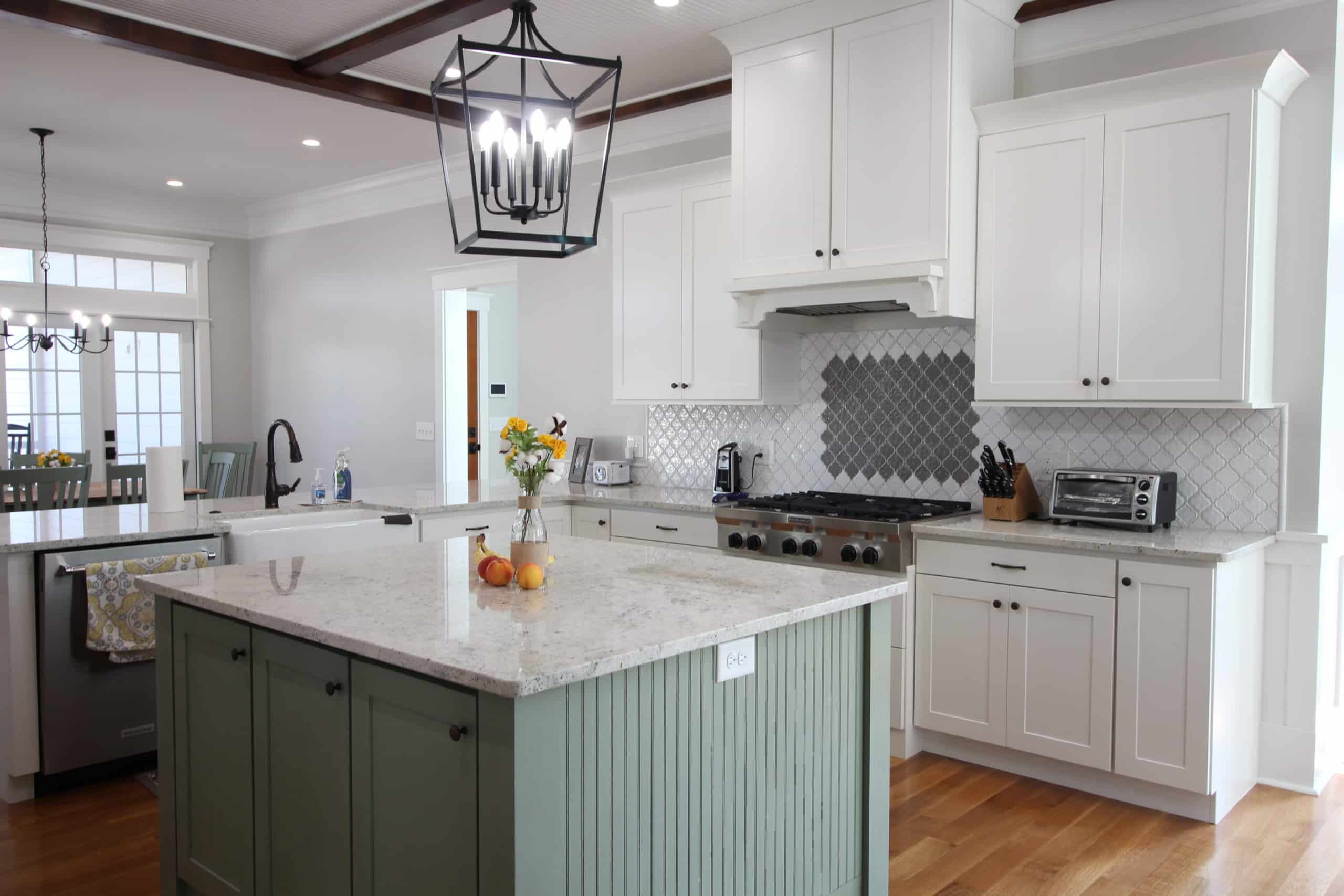 Modern kitchen with white cabinets, gray backsplash, stainless appliances, green island, marble countertop, wood floors, large light fixture.
