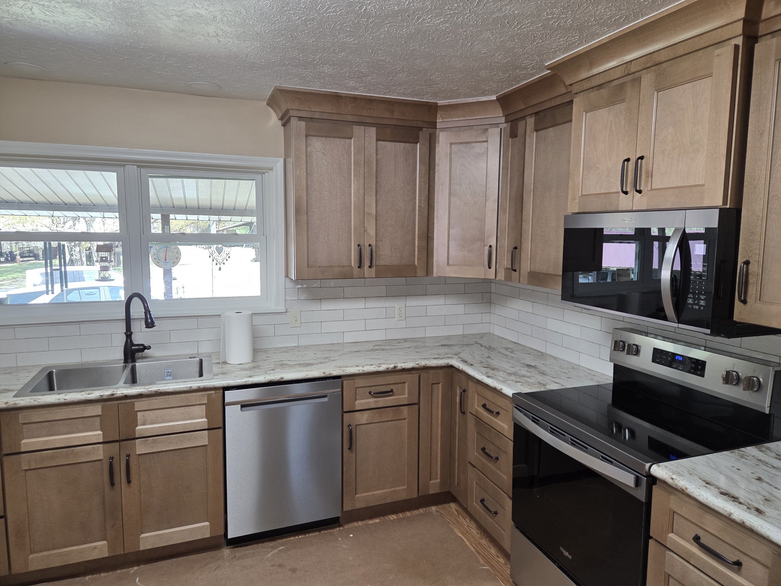 Modern kitchen with wood cabinets, stainless steel appliances, white marble countertops, a double window above the sink, white subway tile backsplash, and a paper towel roll on the counter.
